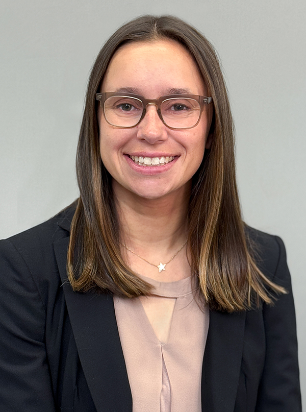 Headshot of Attorney, Emma Stapleton in a black blazer and tan blouse. She is wearing glasses and smiling.
